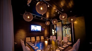 A conference room with a long table set for a meeting, a television screen, and unique spherical hanging lights.