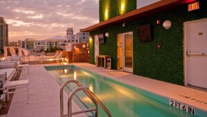 A rooftop pool area with lounge chairs, a pool with a depth marker, and an exit sign.