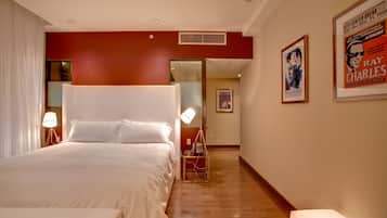 A hotel room with a large bed, bedside lamps, a poster on the wall, and a wooden floor.
