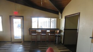 A room with a wooden floor, a red chair, a kitchen area with a refrigerator, and a window with a view of buildings. - Americas Best Value Inn Story City (Story City)