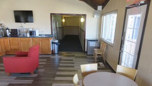 A hotel lobby with a wooden floor, a red sofa, a round table with chairs, a TV mounted on the wall, and a trash bin. - Americas Best Value Inn Story City (Story City)
