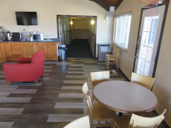 A hotel lobby with a wooden floor, a red sofa, a round table with chairs, a TV mounted on the wall, and a trash bin. - Americas Best Value Inn Story City (Story City)