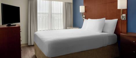 A hotel room with a large bed, a TV on a wooden dresser, and a window with curtains.
