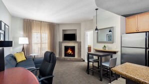A modern living room with a fireplace, a dining area, and a kitchen with a refrigerator. - Residence Inn Phoenix NW/Surprise (Surprise)