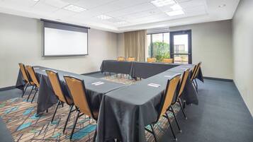 A conference room with a long table, chairs, a projector screen, and a carpeted floor.