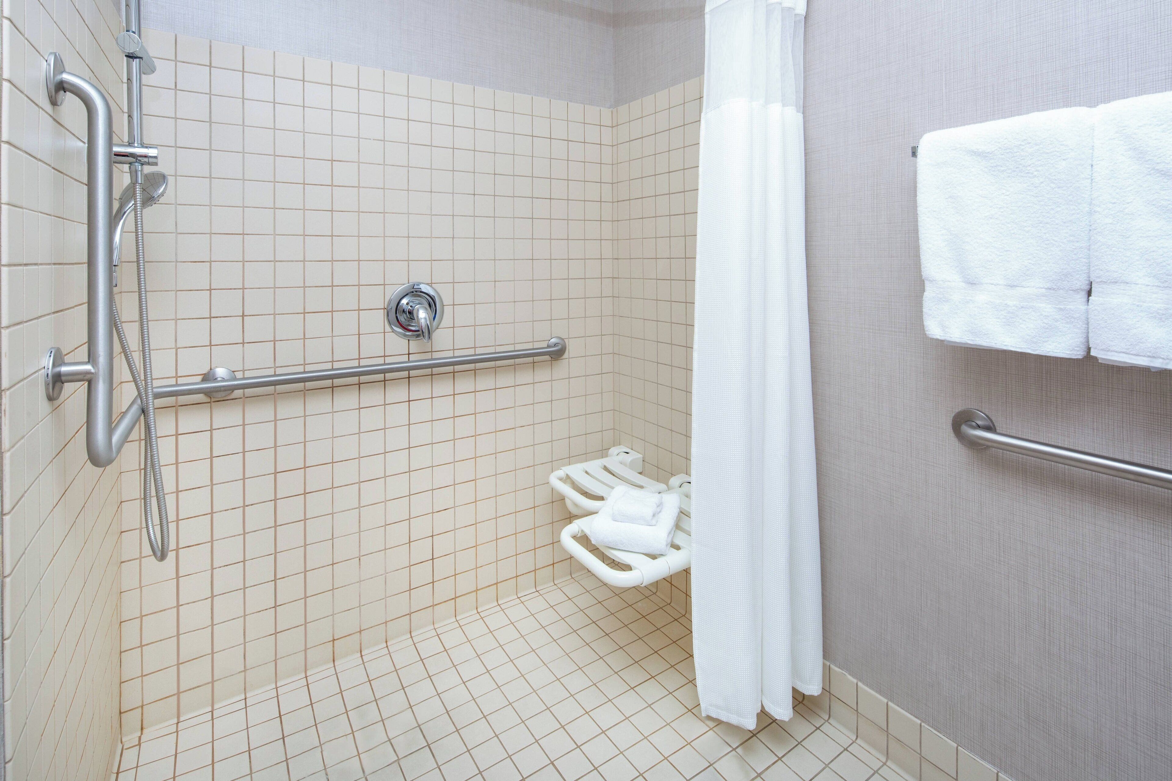 A bathroom with a shower, grab bars, a towel rack, and a toilet with a grab bar.