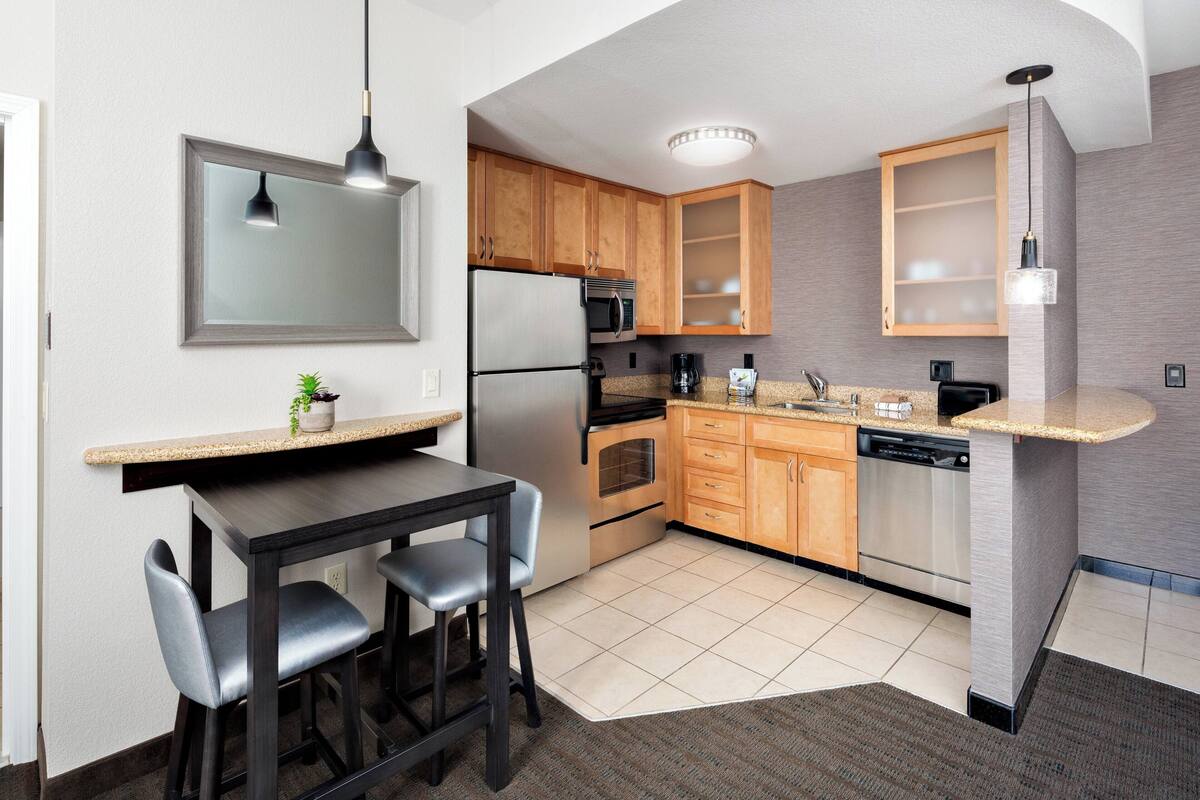 A modern kitchen with wooden cabinets, stainless steel appliances, a granite countertop, and a bar area with stools.