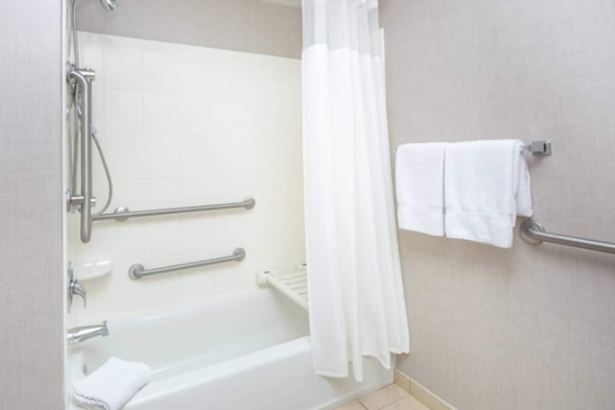 A bathroom with a bathtub, a shower, grab bars, and a towel rack.