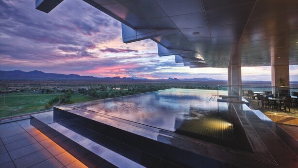 A modern infinity pool with a view of mountains and a sunset.