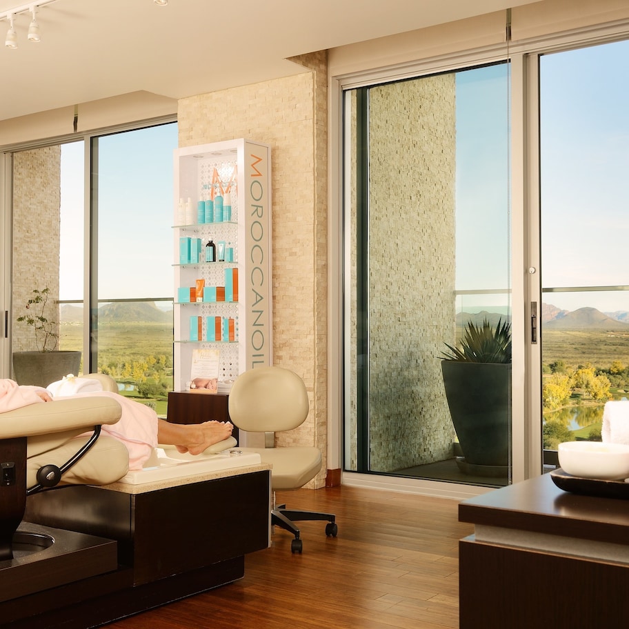 A spa room with a massage chair, a shelf with spa products, and a view of the landscape through large windows.