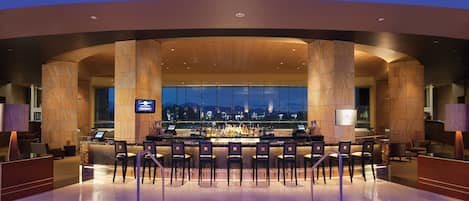 A bar area with a view of the cityscape at night, featuring a modern design with wooden accents and a glass partition.