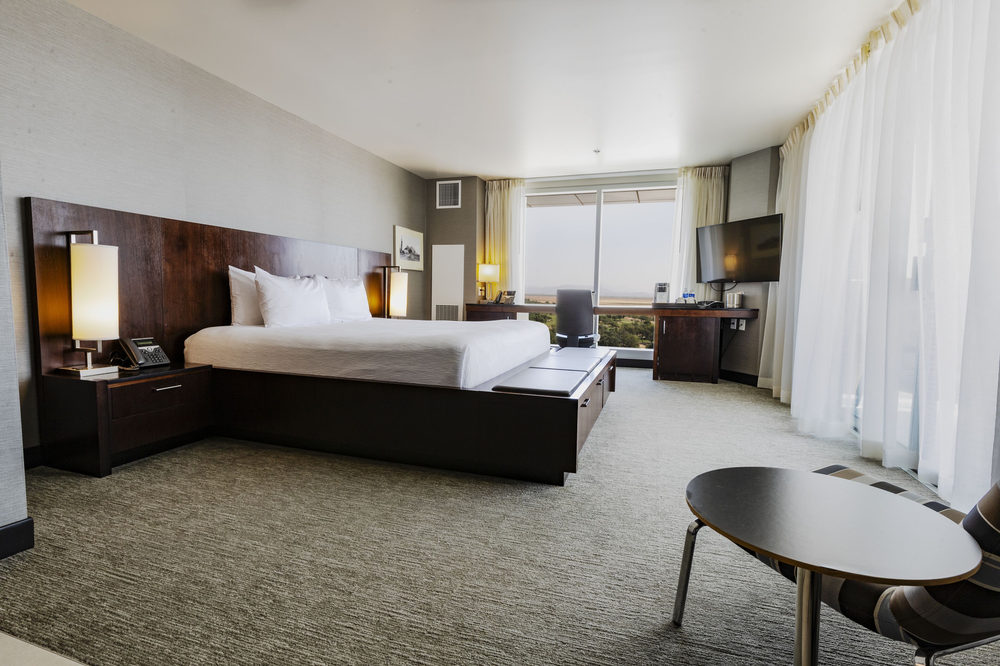 A hotel room with a large bed, a desk with a chair, a TV, and a view of the outdoors.