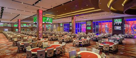 A large banquet hall with multiple round tables and chairs, equipped with card tables and electronic devices.