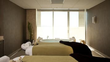Un cuarto de spa con dos camas, una bañera y un ventanal grande.