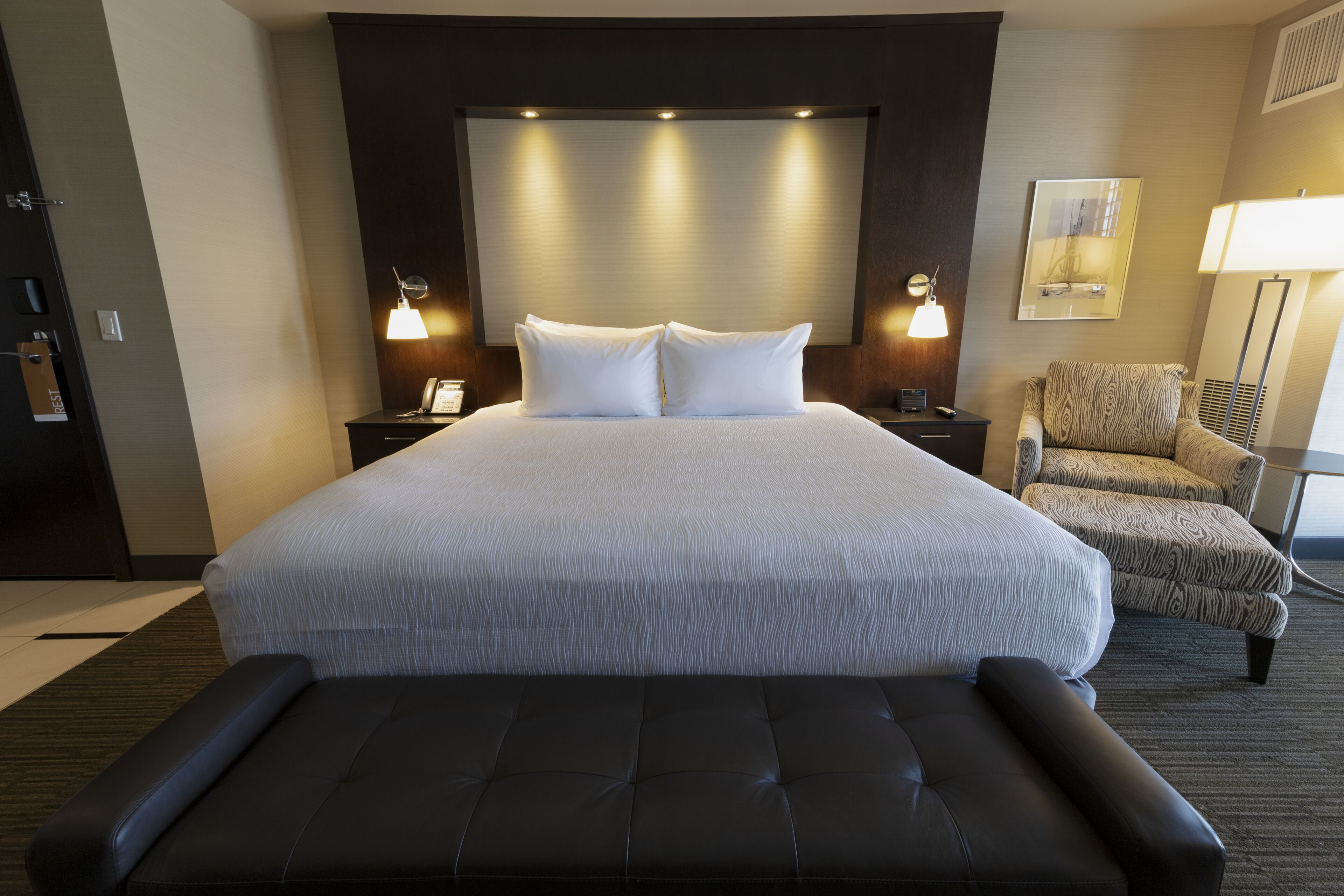 A hotel room with a large bed, two bedside lamps, a chair, and a bedside table.
