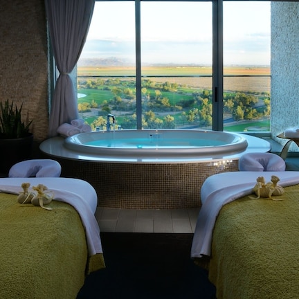A spa room with two beds, a large window offering a view of a golf course, and a hot tub.