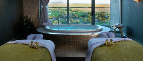 Un cuarto de spa con dos camas, un ventanal que ofrece vistas a un campo de golf y una bañera de hidromasaje.