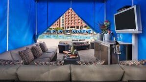 A poolside lounge with a view of a hotel building, a TV, and a bar area with a bottle of champagne.