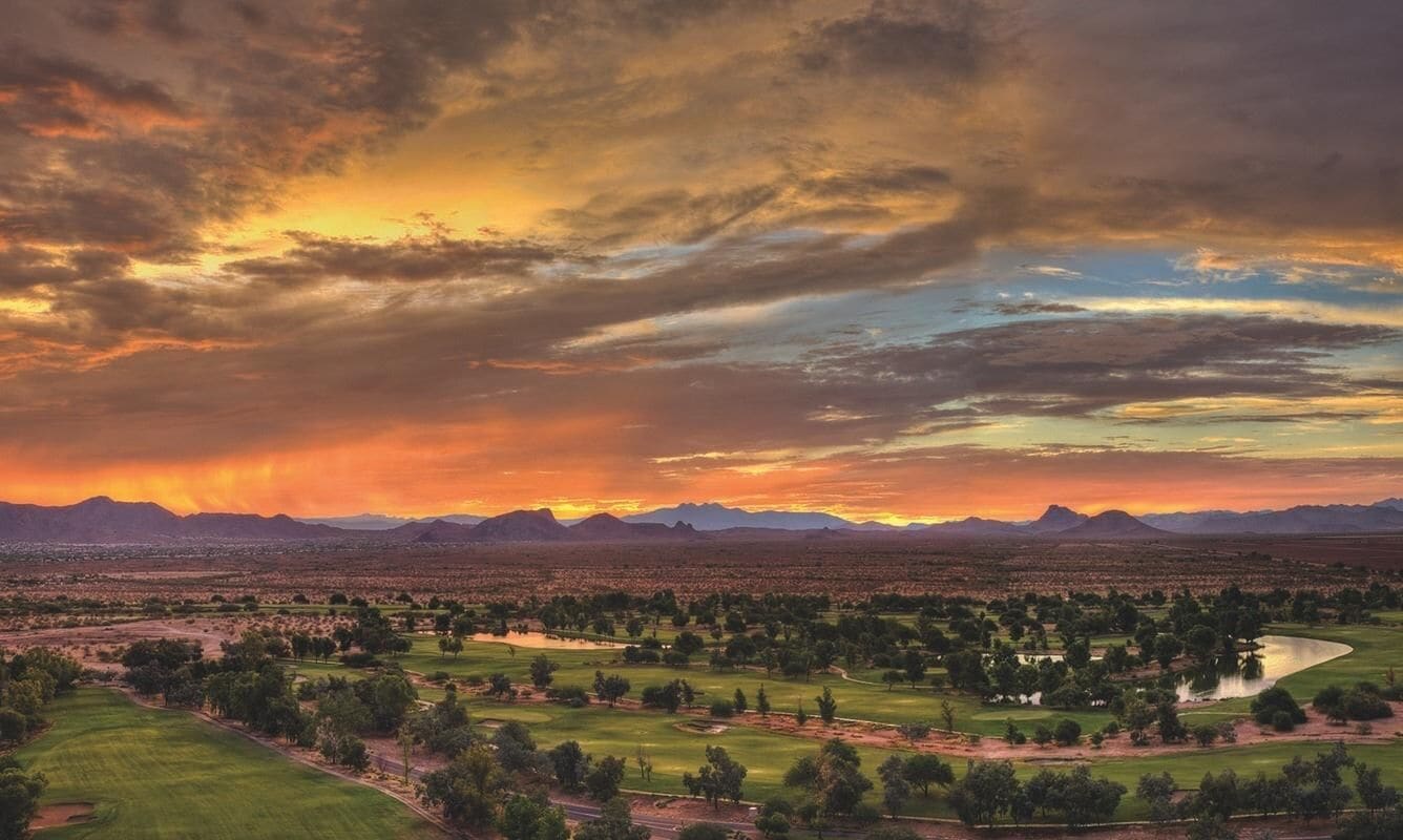 A golf course with a panoramic view of mountains and a sunset.