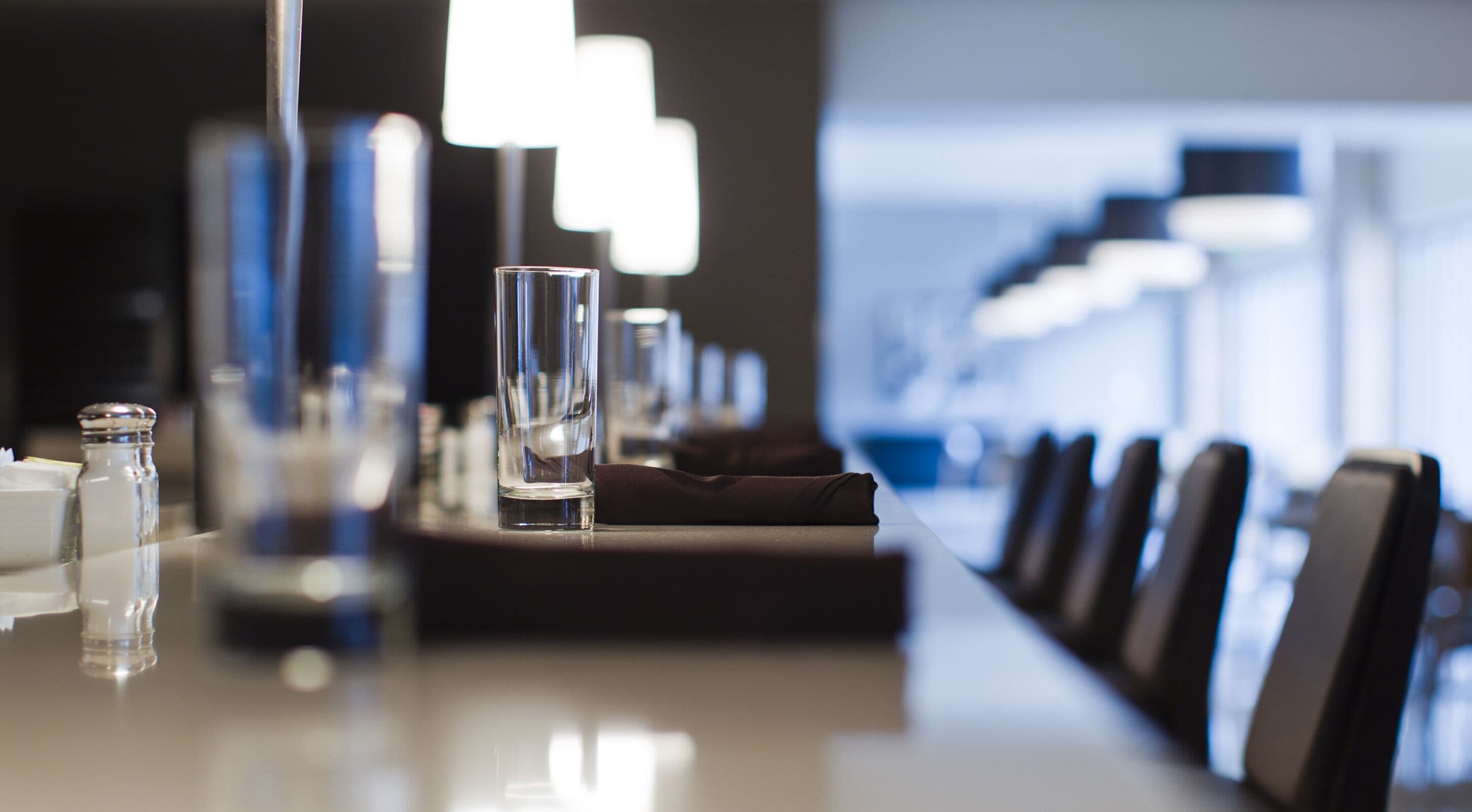 A modern hotel conference room with a long table, chairs, and a row of lamps.