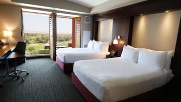 A hotel room with two beds, a desk, and a view of the outdoors.