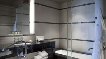 A modern bathroom with a glass shower enclosure, a black countertop sink, and a white bathtub.