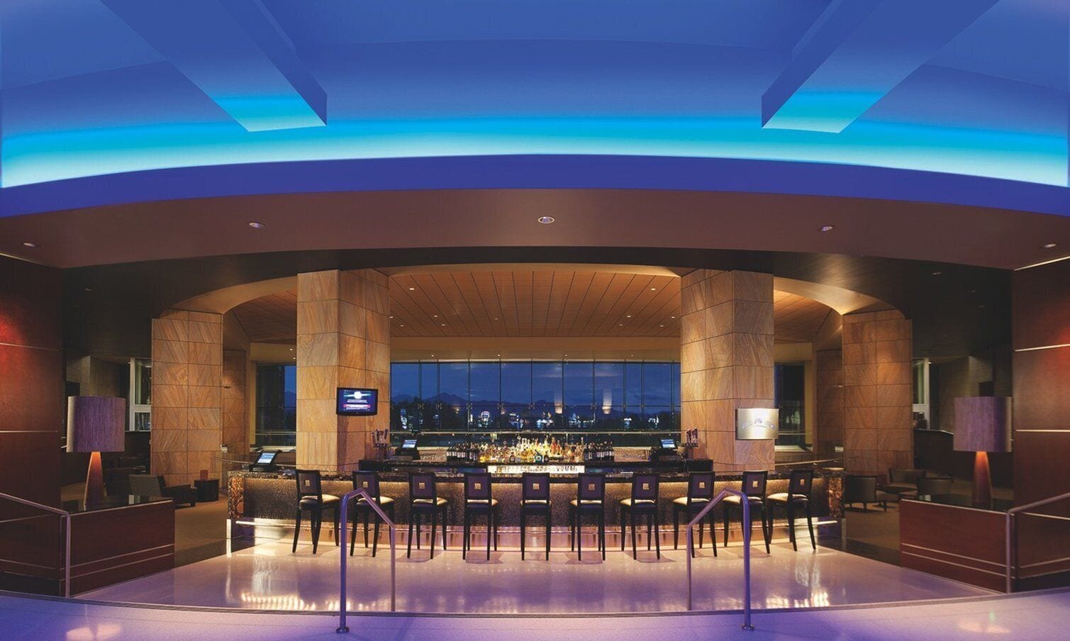 A modern bar area with a long counter, multiple bar stools, and a television screen.