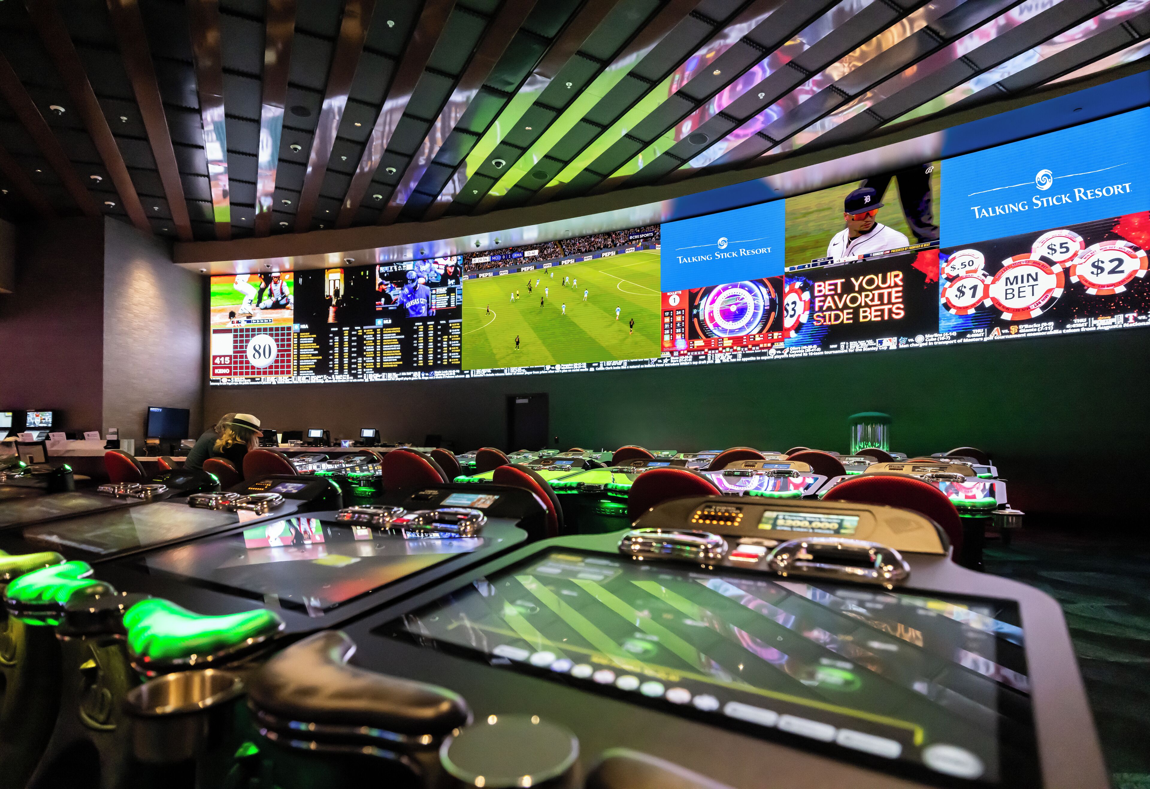 A casino with multiple gaming tables and large screens displaying sports events.