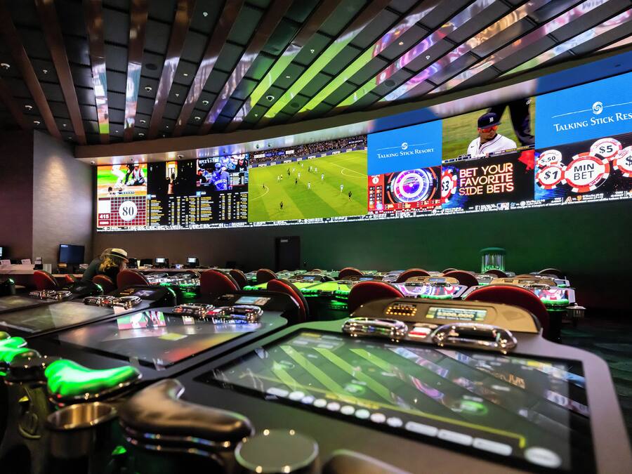 A casino with multiple gaming tables and large screens displaying sports events.