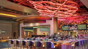 A modern bar area with a unique ceiling design, a bar counter with multiple screens, and a patterned carpet.