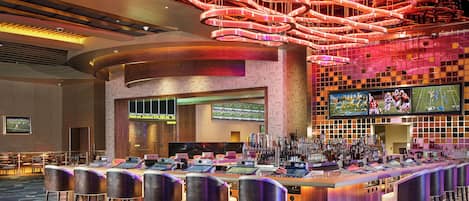 A modern bar area with a unique ceiling design, a bar counter with multiple screens, and a patterned carpet.