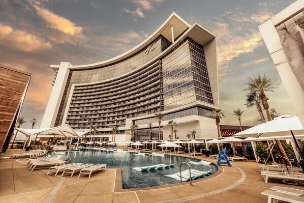 Un hotel con una piscina grande, tumbonas, sombrillas y palmeras.
