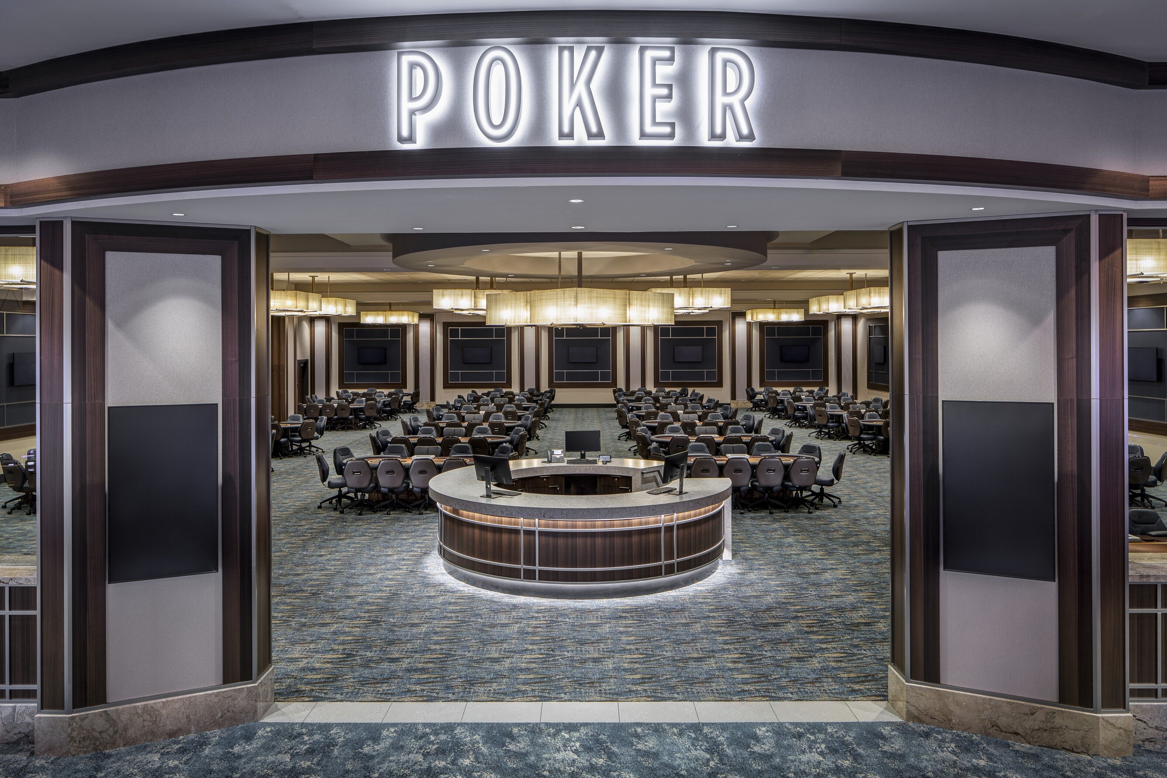 Ein Pokerraum mit einem großen runden Tisch, mehreren Stühlen und einem 'POKER'-Schild darüber.