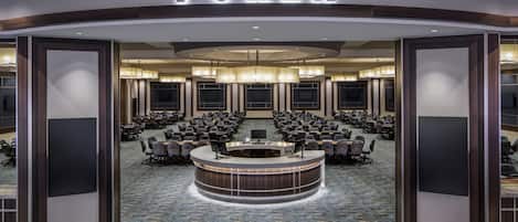 Uma sala de pôquer com uma grande mesa circular, várias cadeiras e um letreiro com a palavra 'POKER'.