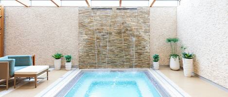 A swimming pool with a stone wall, lounge chairs, and potted plants.