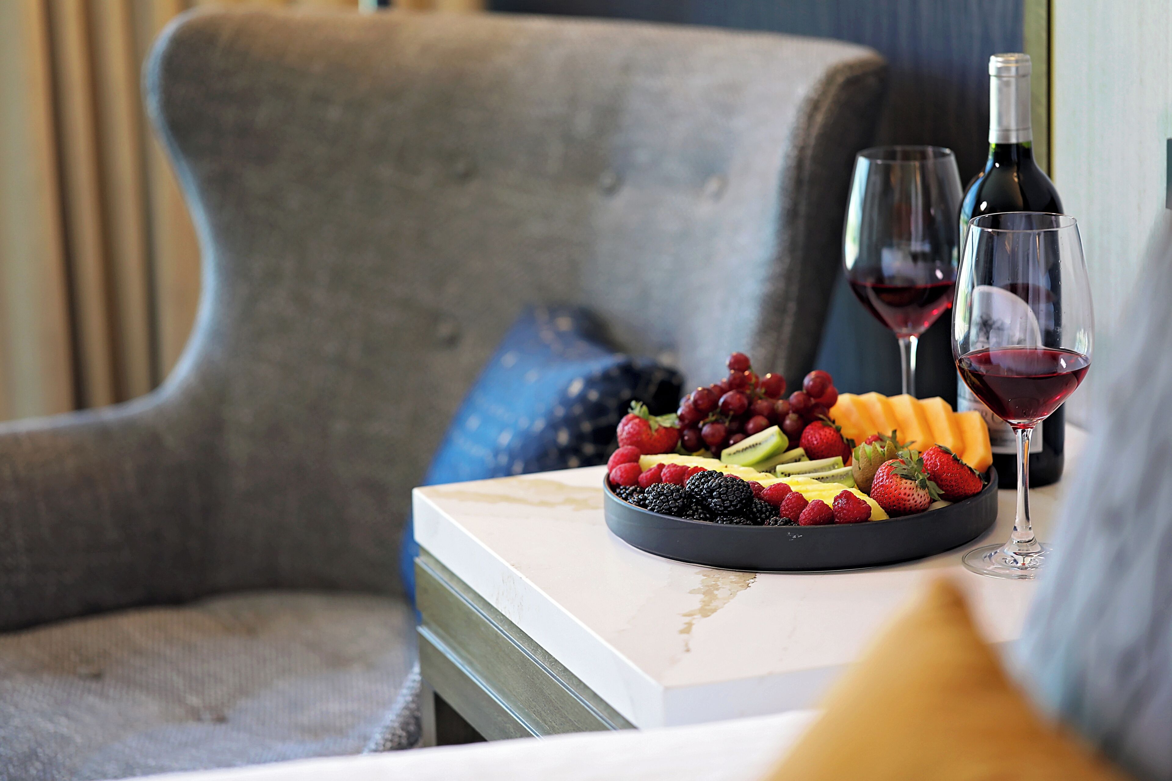 Un vassoio di frutta con bicchieri da vino su un tavolo, una sedia e un divano sullo sfondo.
