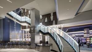 A modern lobby with a curved staircase, a bar area, and a gaming arcade. - Choctaw Casino & Resort Durant, a Wyndham Grand Hotel (Durant)