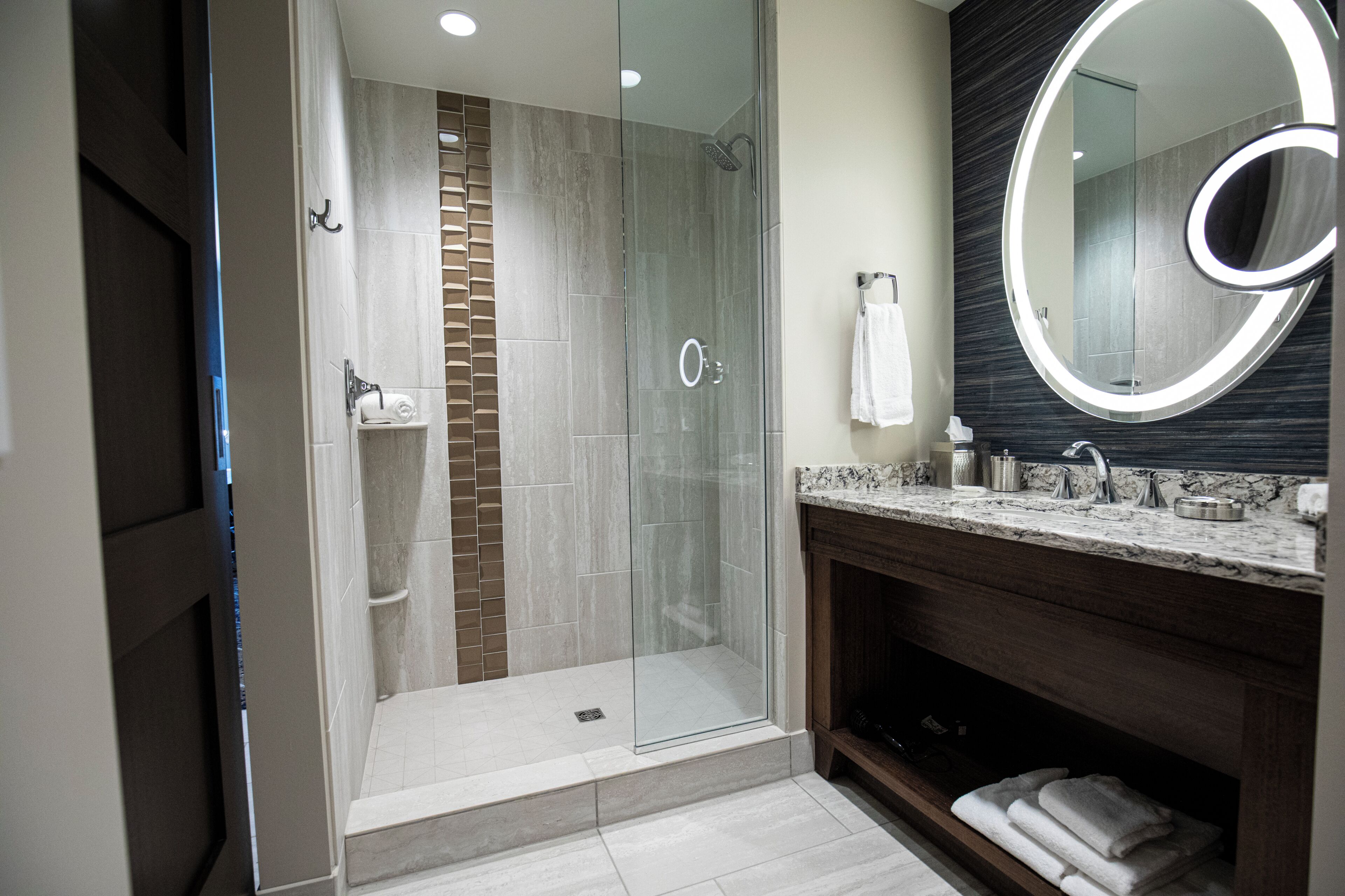 Un baño moderno con ducha envuelta en vidrio, lavamanos de mármol y un espejo grande.