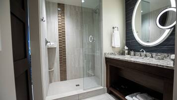 Un baño moderno con ducha envuelta en vidrio, lavamanos de mármol y un espejo grande.