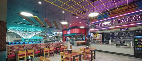 Interior de un restaurante con cabinas, mesas y un letrero de neón para Velvet Taco.