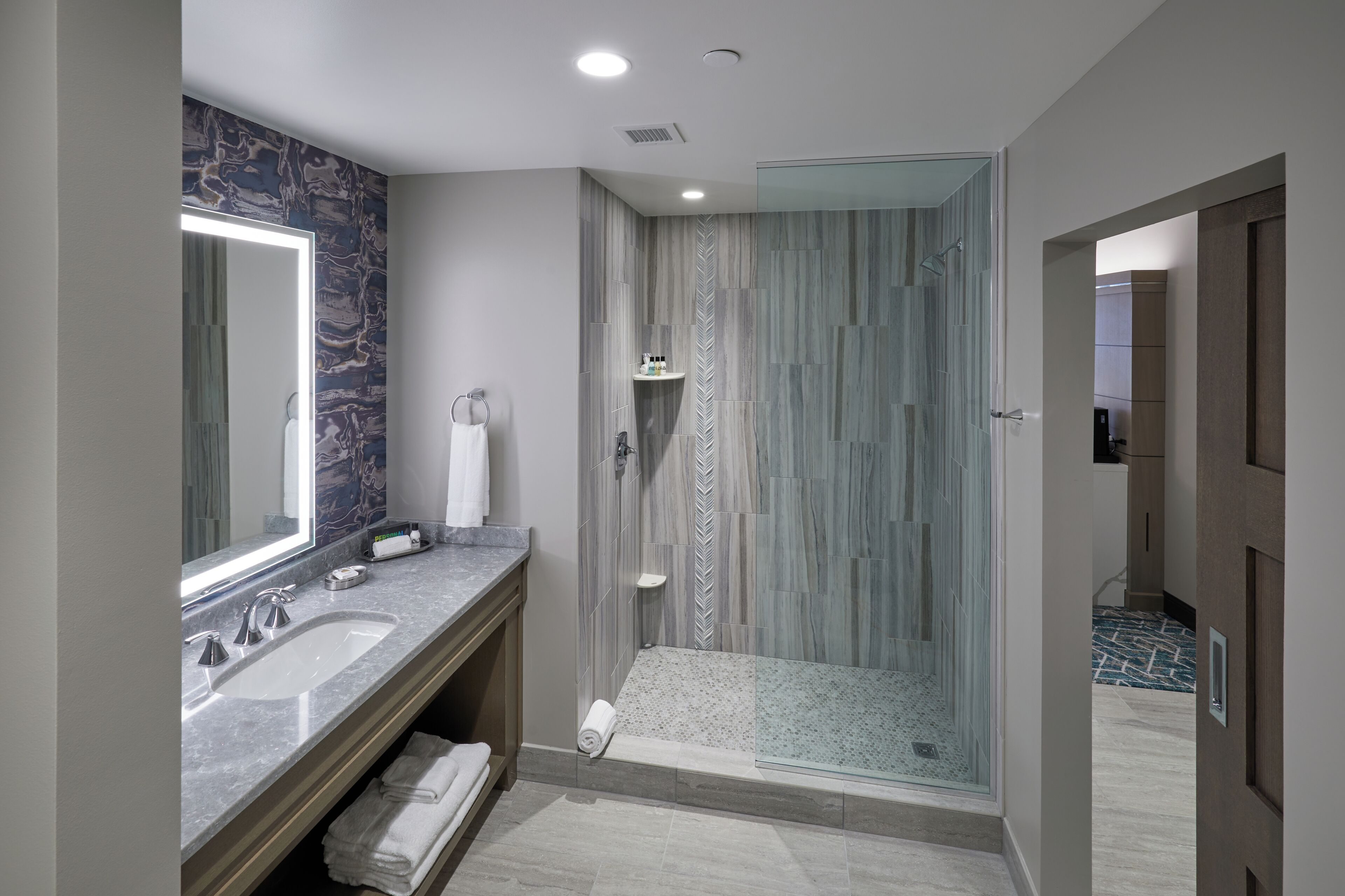 Un baño moderno con un espejo grande, dos lavamanos, una ducha y zona de ducha con mampara de vidrio.