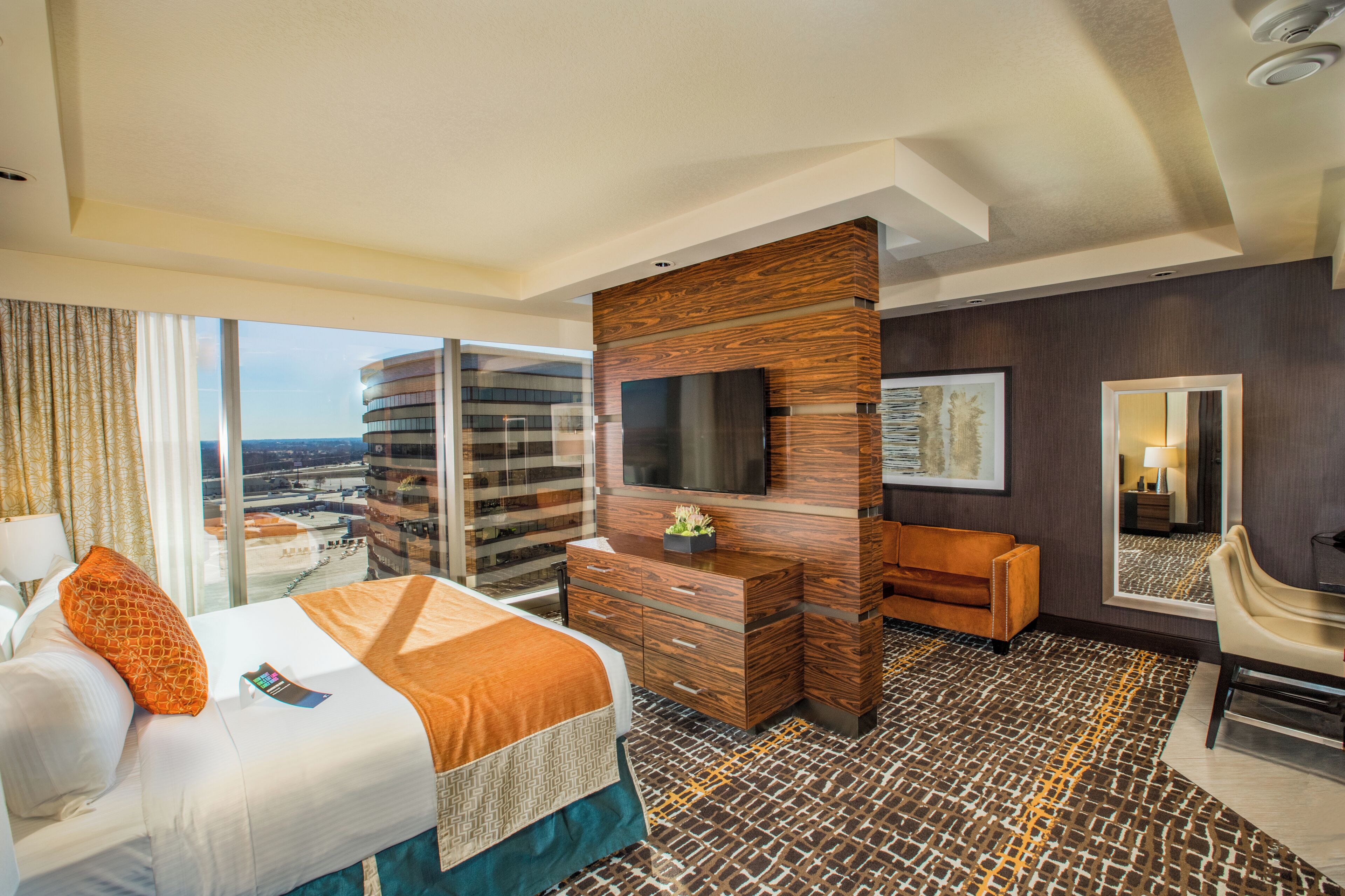 A hotel room with a bed, a TV, a desk, and a large window offering a city view.