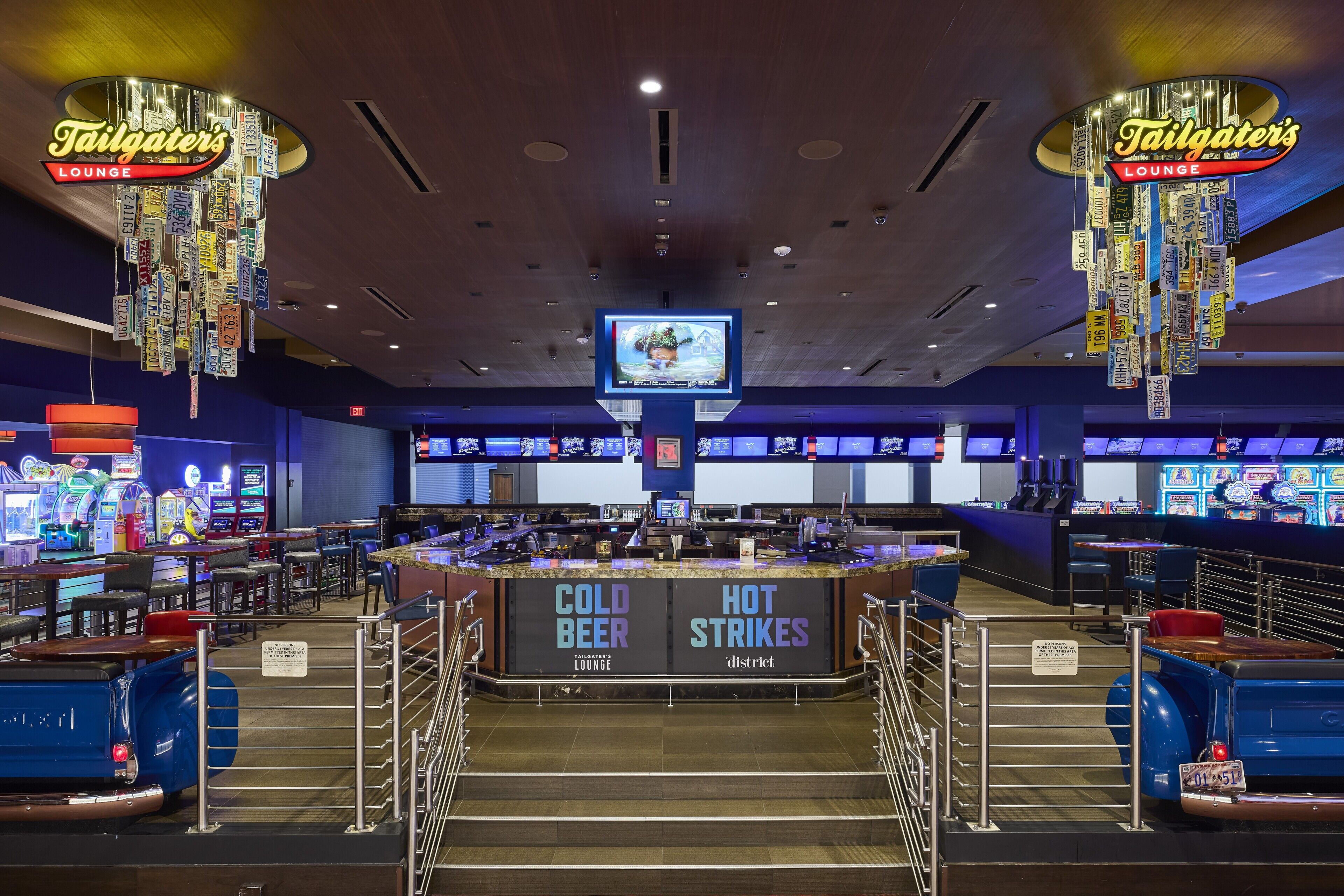 Eine Casino-Lounge mit Barbereich, der mit 'COLD BEER' und 'HOT STRIKES' beschriftet ist, sowie Spielhallenspielen und einem Fernsehbildschirm.