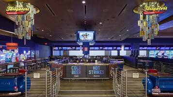A casino lounge with a bar area labeled 'COLD BEER' and 'HOT STRIKES,' arcade games, and a television screen.