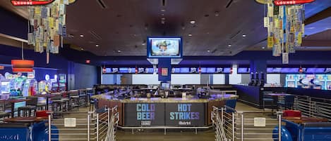 A casino lounge with a bar area labeled 'COLD BEER' and 'HOT STRIKES,' arcade games, and a television screen.