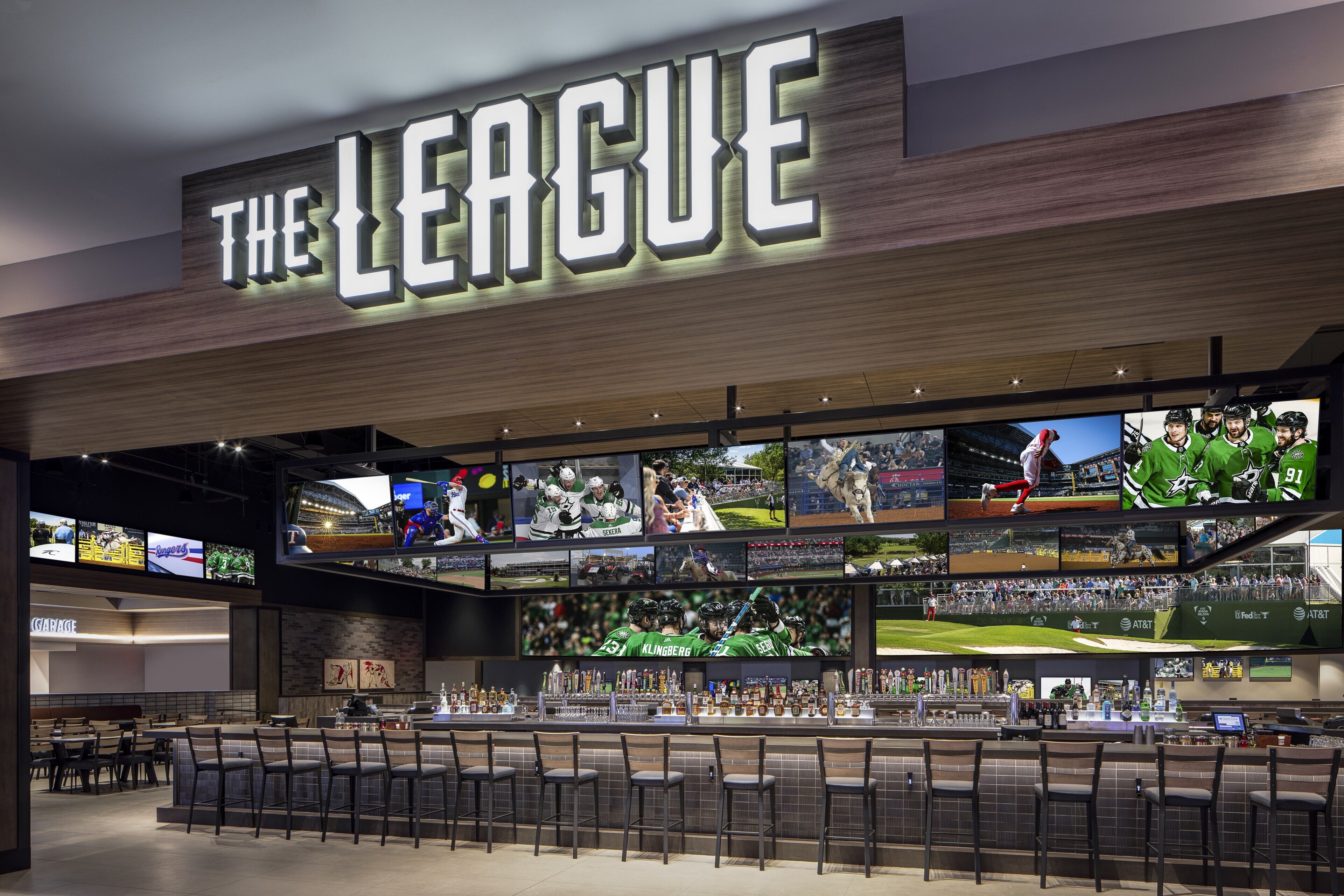 Een sportbar genaamd 'The League' met meerdere schermen waarop sportevenementen te zien zijn, een bargedeelte met krukken en een goed zichtbaar bord.