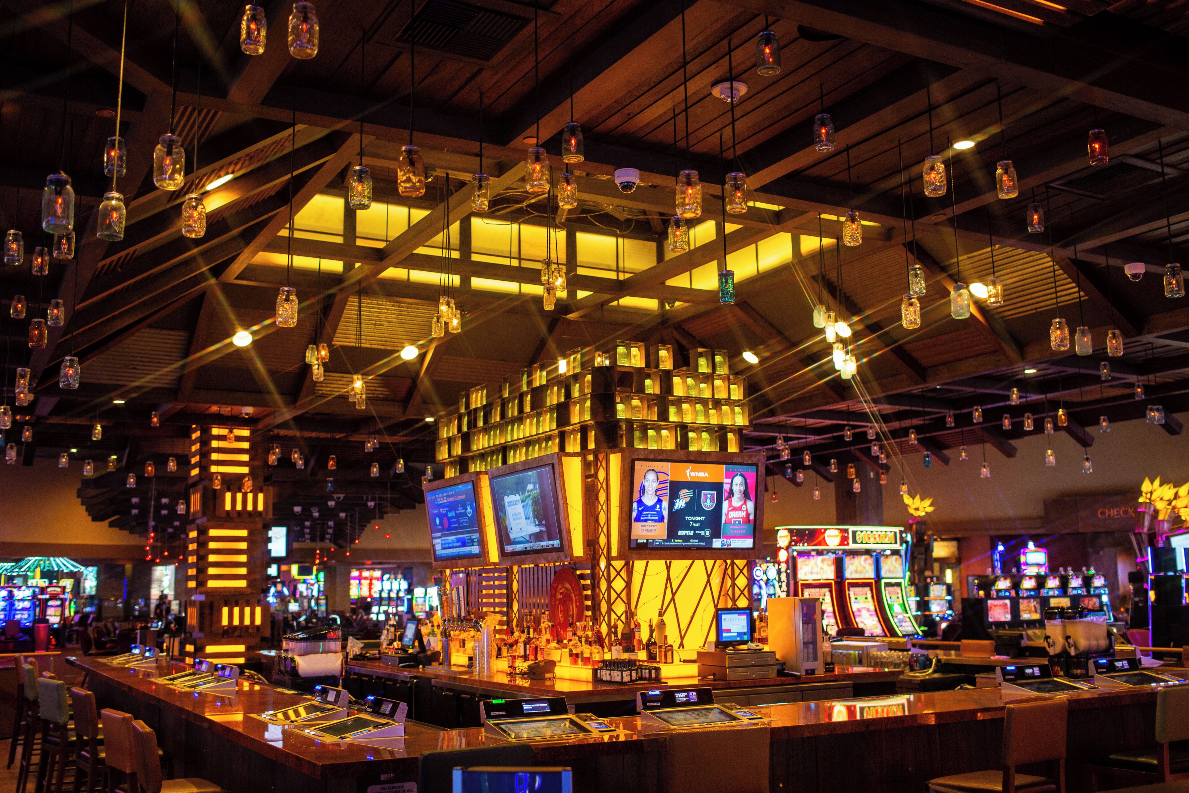 A bar area with multiple gaming machines, a bar counter, and hanging light fixtures.