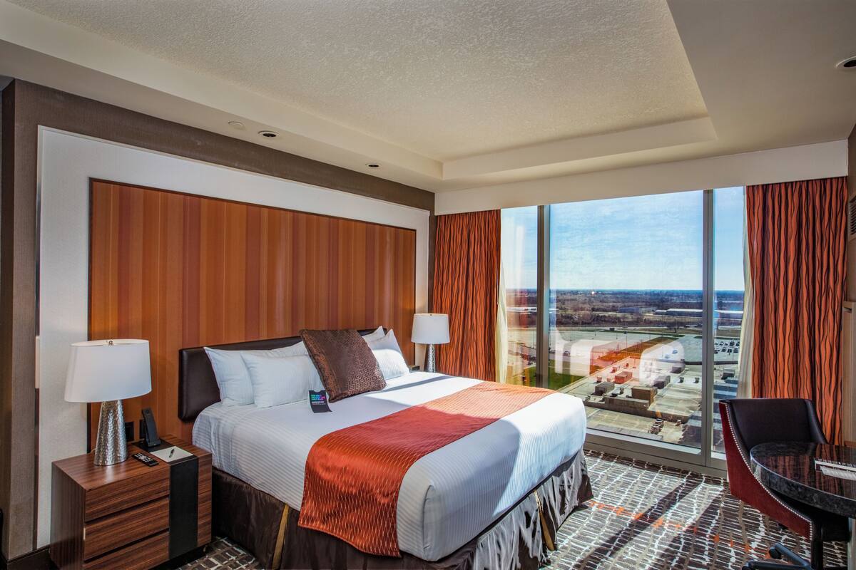 Habitació d'hotel amb un llit gran, dues taules de nit, un escriptori amb cadira i una finestra ampla que ofereix vista a la ciutat.
