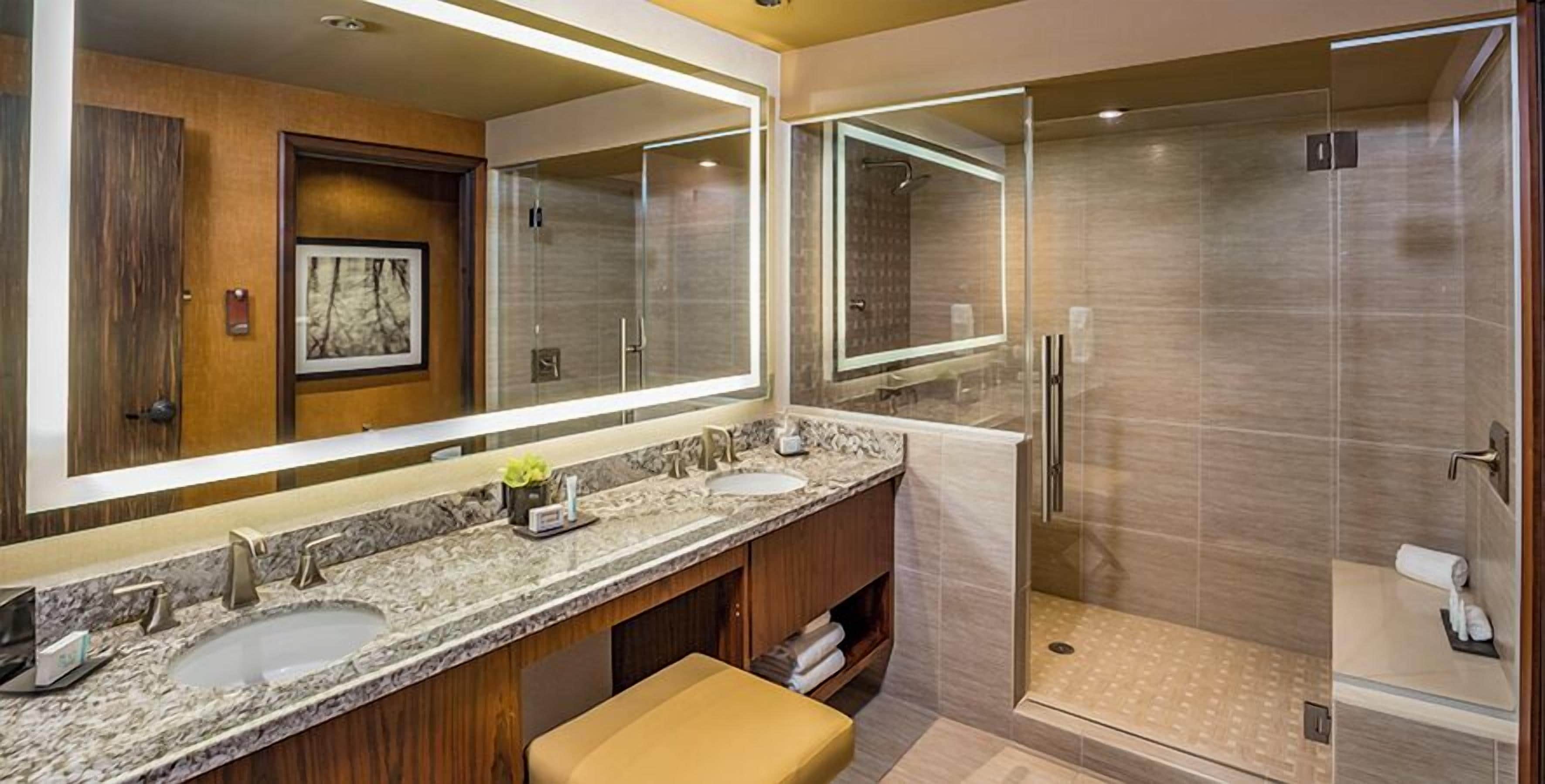 A modern bathroom with two sinks, a large mirror, and a walk-in shower.