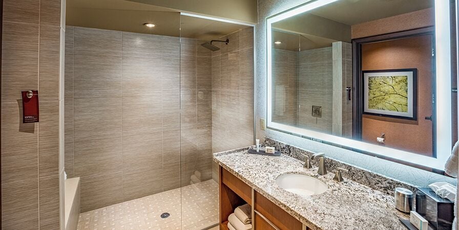A modern bathroom with a glass-enclosed shower, a large mirror, and a marble countertop.